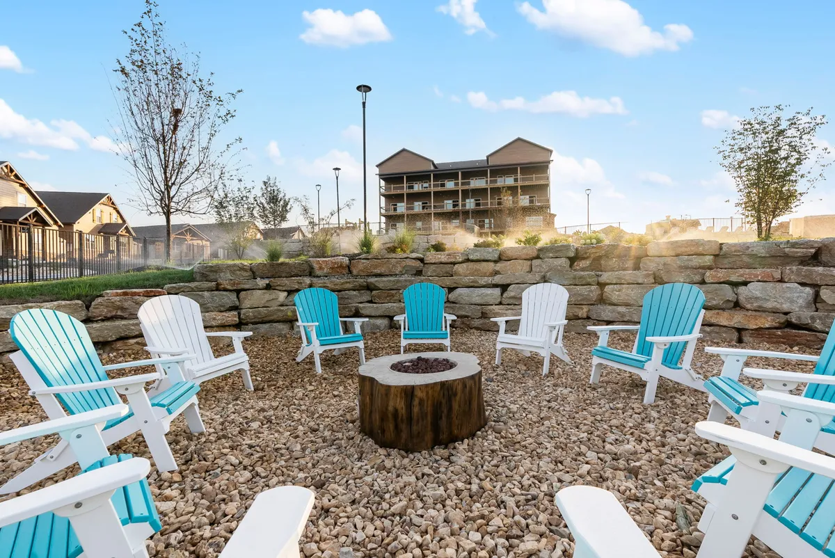 An inviting fire pit area surrounded by Adirondack chairs and enhanced landscaping, set against the colors of a sunset sky. The arrangement encourages communal gatherings and cozy evenings outdoors, perfectly placed for making s'mores or simply enjoying nature.