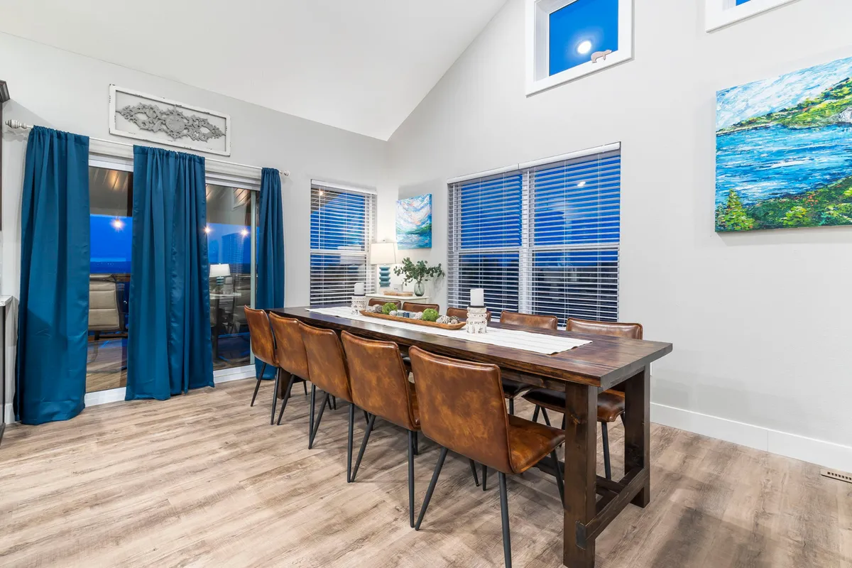 A spacious dining area with a long table set for a group, surrounded by cozy curtains and large windows that let in natural light. Distinctive artwork adorns the walls, and the room feels both stylish and inviting—ideal for shared meals and celebrations.