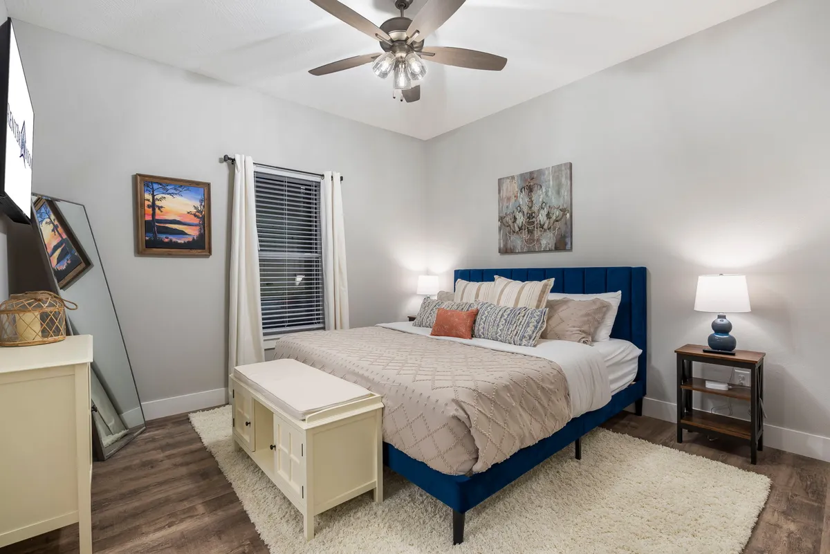 A cozy bedroom with a comfortable bed dressed in premium bedding, decorative pillows, soothing art pieces on the wall, and a nightstand with a warm lamp. The ambiance is serene and inviting, ideal for relaxation and unwinding.