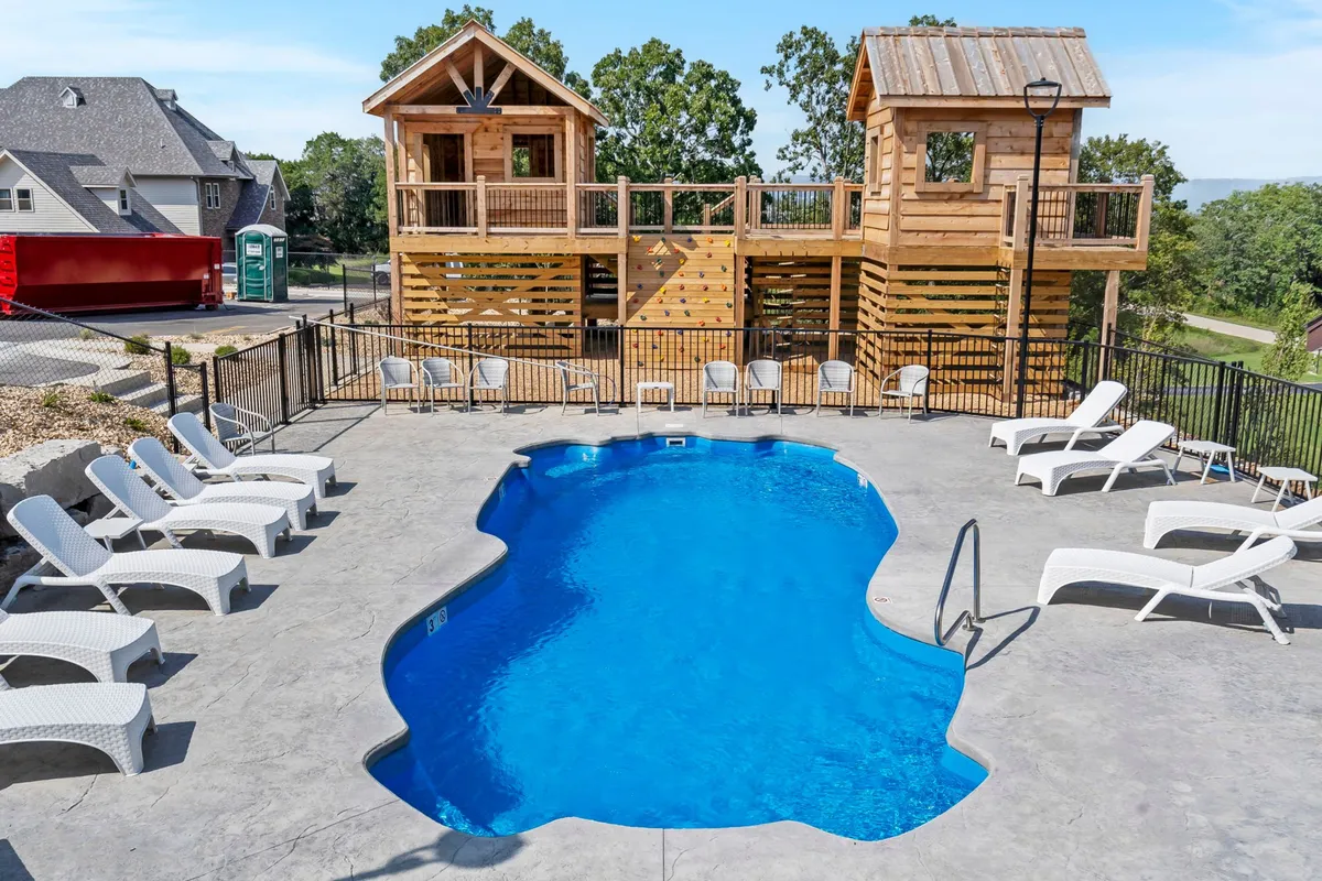 An inviting exterior shot of a swimming pool adjacent to wooden playhouses, with lounge chairs nearby. The space is alive with children playing and adults enjoying the sun, providing both recreational and relaxation opportunities.