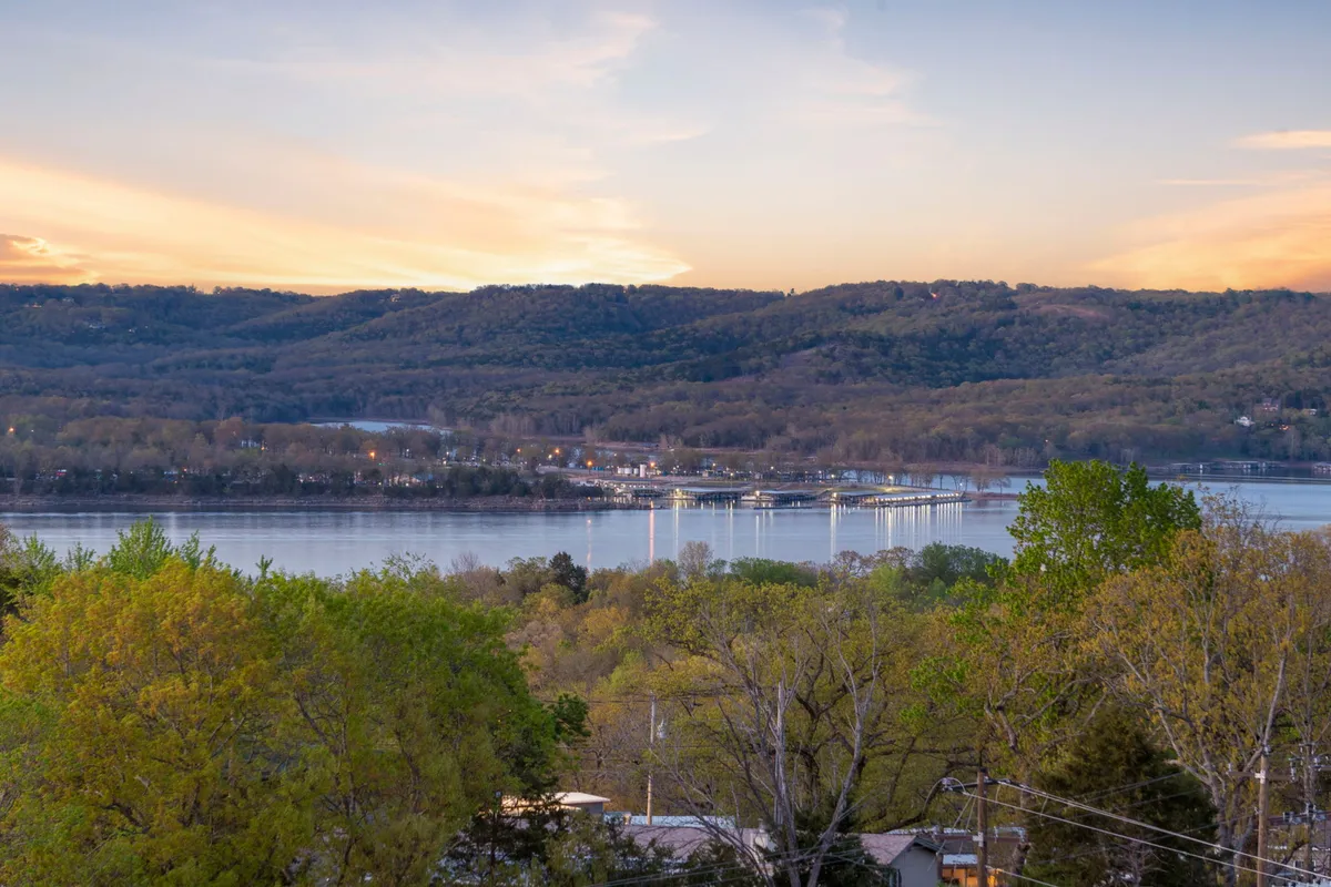 A breathtaking view of Table Rock Lake at sunset, with tranquil water reflecting the sky and rolling hills in the background. The scene radiates peace and invites thoughts of boating, fishing, and absorbing the natural beauty of the Ozarks.