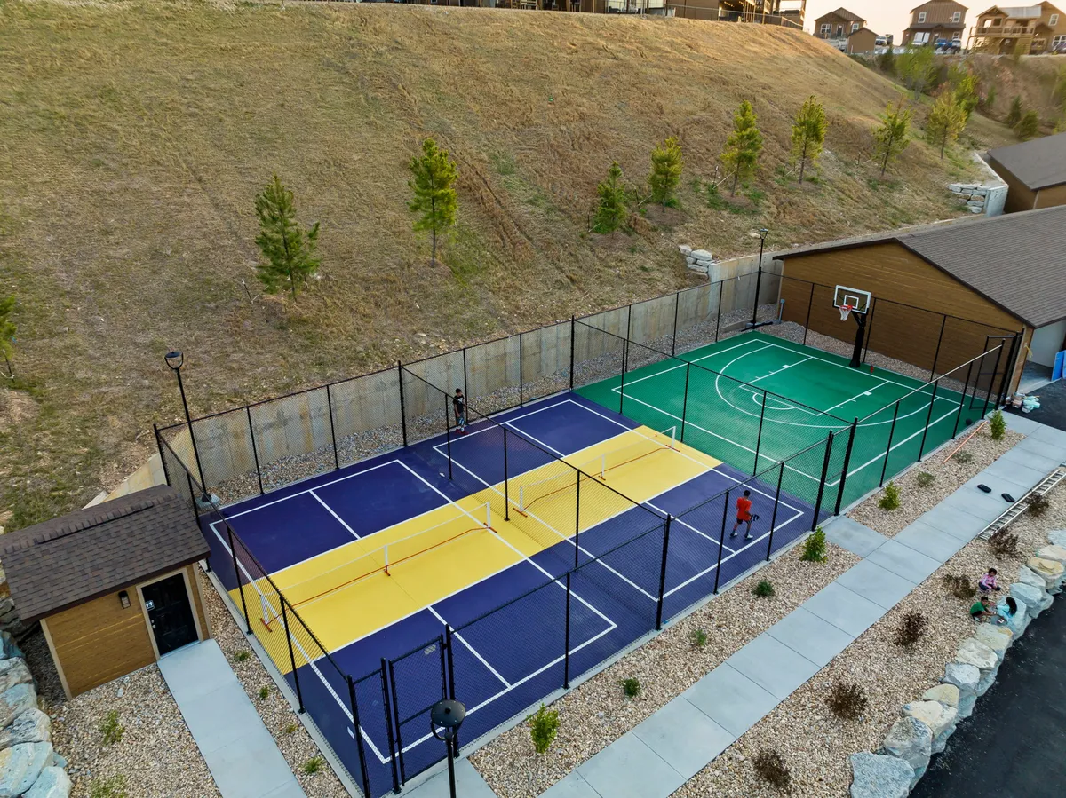 A dynamic outdoor multi-sport court equipped for basketball and pickleball, set against a scenic landscaped backdrop. The image evokes energy and opportunity for friendly competition and group activities.