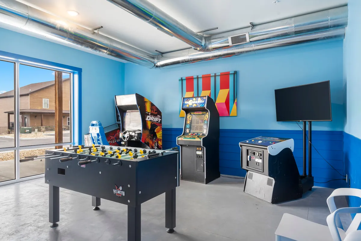 This image captures a lively game room with a foosball table, arcade machines, colorful wall art, and a television. The space is energetic and inviting, perfect for friendly competition and group entertainment.