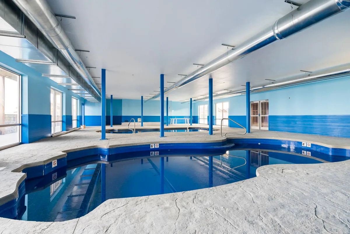 A spacious indoor pool area with blue walls and large windows allowing natural light to flood the space. Poolside lounging areas promise year-round aquatic enjoyment, whether for a refreshing swim or gathering with friends and family.