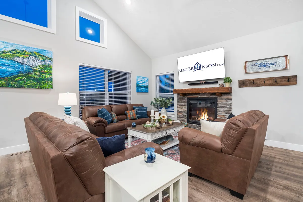 A warm, welcoming living room with a glowing electric fireplace as its centerpiece. The space features plush sofas arranged for conversation, a coffee table, and tasteful artwork on the walls, all bathed in cozy ambient light—perfect for intimate gatherings or quiet moments.