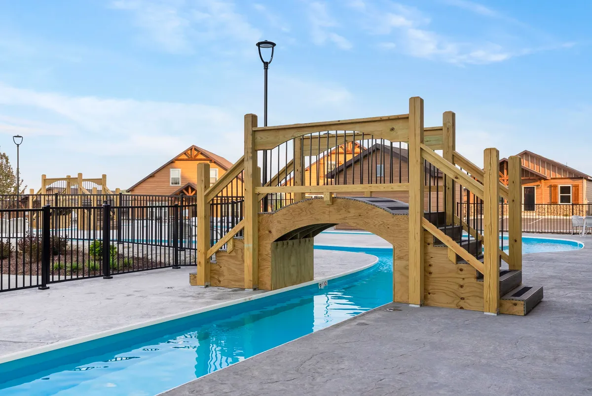 An exterior view features a wooden bridge arching over a swimming pool, surrounded by cabins and landscaped greenery. The inviting setting captures both poolside relaxation and memorable family gatherings, with the bridge offering a distinctive visual link to the 'bridge views' mentioned in the narrative.