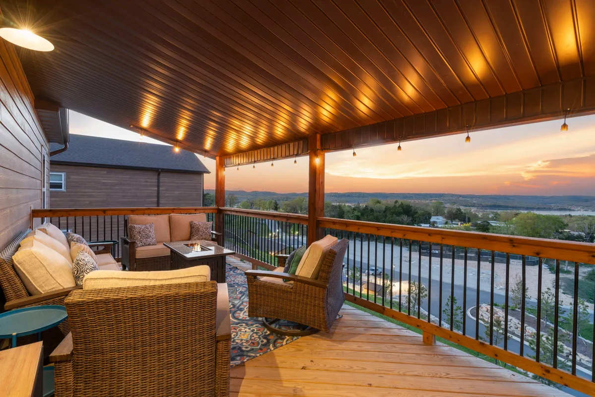 A cozy exterior deck seating area is arranged with comfortable chairs and a decorative rug, perfectly positioned to watch a stunning sunset over the Ozark landscape. The tranquil setting is ideal for quiet reflection or intimate gatherings with friends or family.